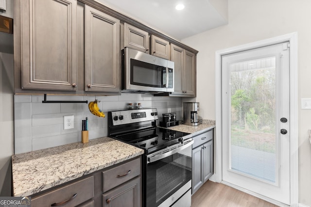 kitchen featuring tasteful backsplash, light wood-type flooring, dark brown cabinetry, appliances with stainless steel finishes, and light stone countertops