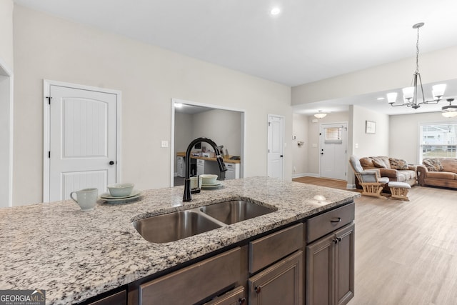 kitchen with light wood-style flooring, a sink, a notable chandelier, light stone counters, and hanging light fixtures