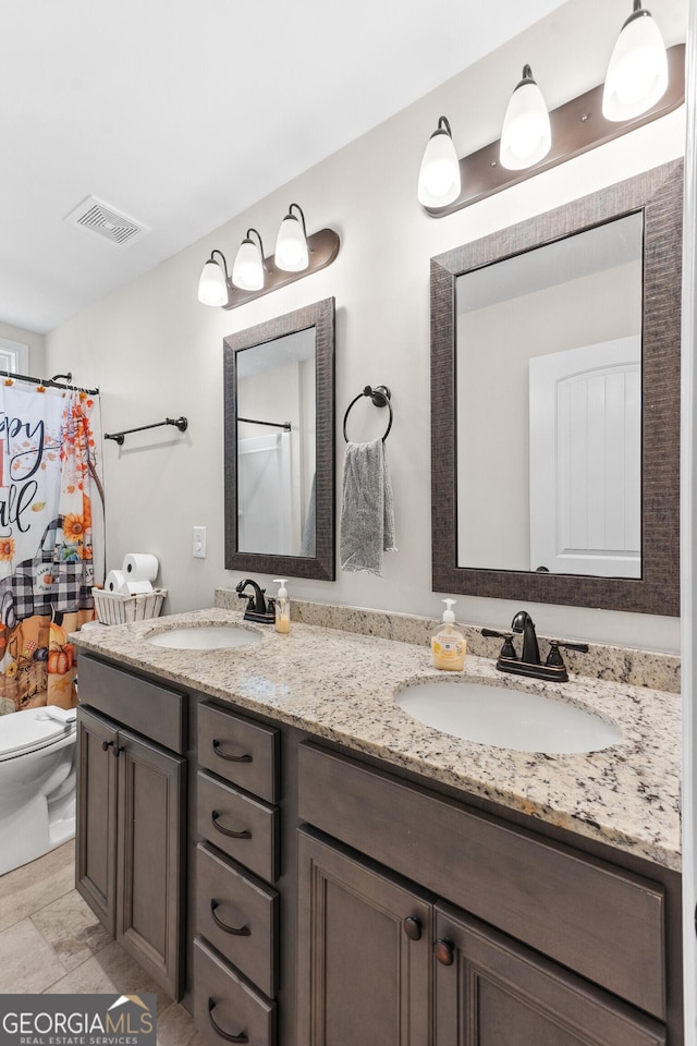 bathroom featuring toilet, a sink, visible vents, and double vanity