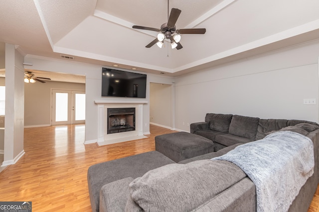 living room featuring ceiling fan, light wood finished floors, a raised ceiling, a fireplace with flush hearth, and visible vents