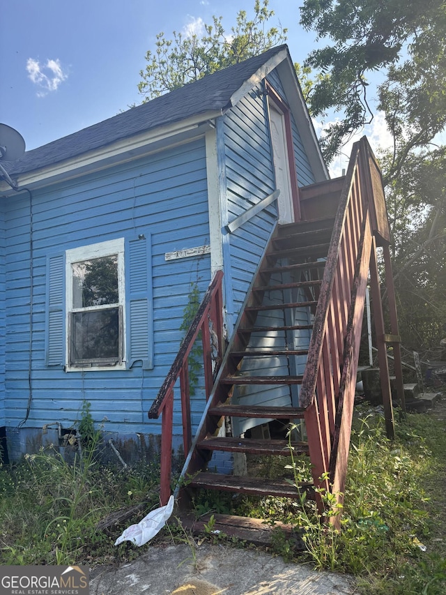 view of property exterior with a shingled roof and stairs