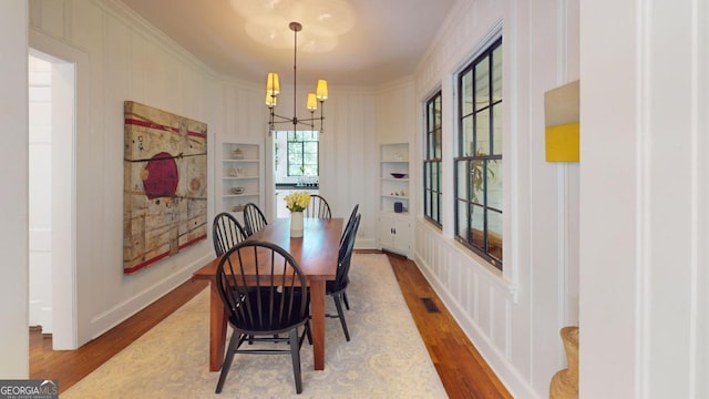 dining room with an inviting chandelier, built in shelves, visible vents, ornamental molding, and wood finished floors