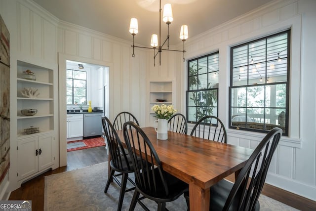 dining area featuring dark wood finished floors, a chandelier, built in shelves, crown molding, and a decorative wall