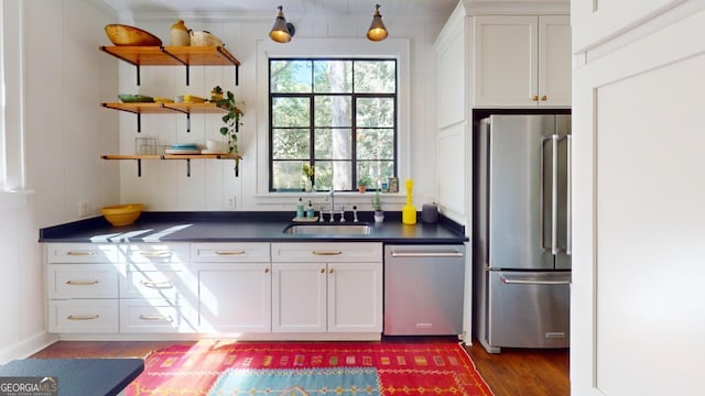 kitchen featuring a sink, white cabinetry, dark countertops, appliances with stainless steel finishes, and wood finished floors