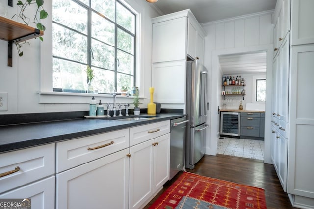 kitchen featuring beverage cooler, dark wood-style floors, dark countertops, a sink, and appliances with stainless steel finishes