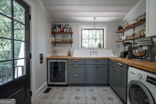 bar with beverage cooler, washer / dryer, ornamental molding, light tile patterned flooring, and a dry bar