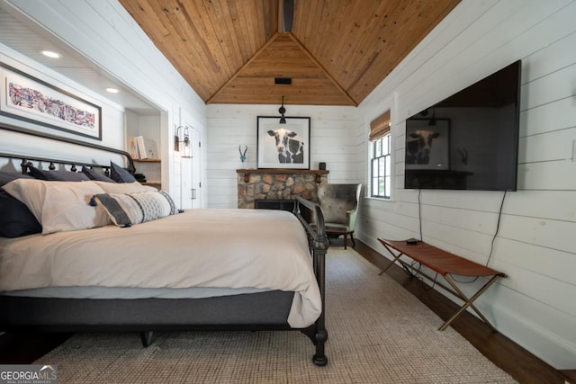 bedroom with a stone fireplace, wood walls, vaulted ceiling, wood ceiling, and wood finished floors