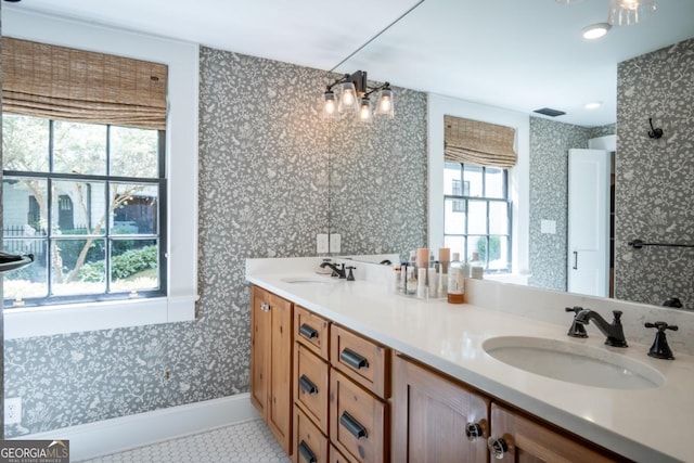 bathroom with a notable chandelier, wallpapered walls, and a sink