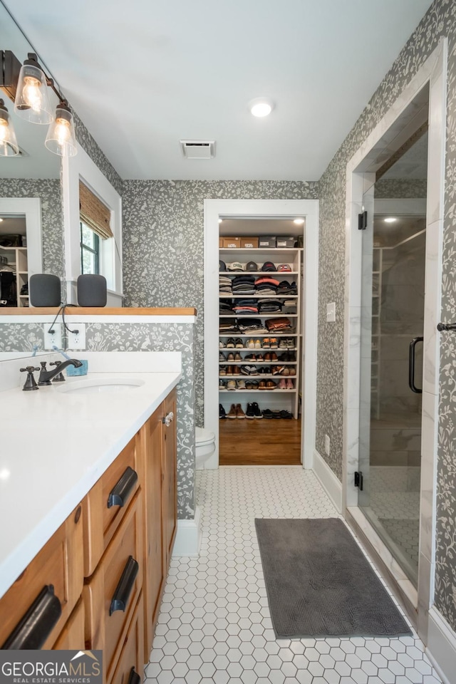 bathroom with a shower stall, visible vents, wallpapered walls, toilet, and vanity