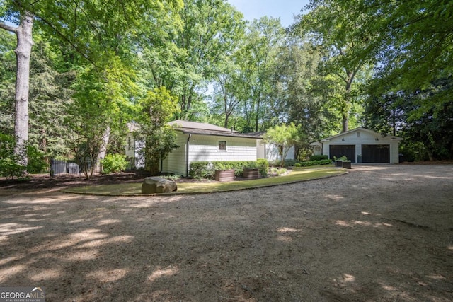 exterior space featuring driveway, fence, a detached garage, and an outbuilding