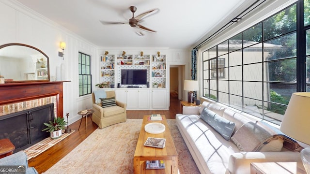 living area featuring a brick fireplace, crown molding, ceiling fan, and wood finished floors