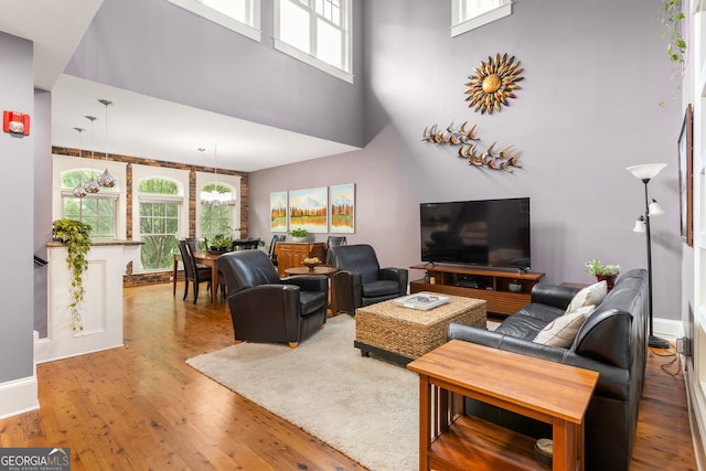 living area with baseboards, wood finished floors, plenty of natural light, and a towering ceiling