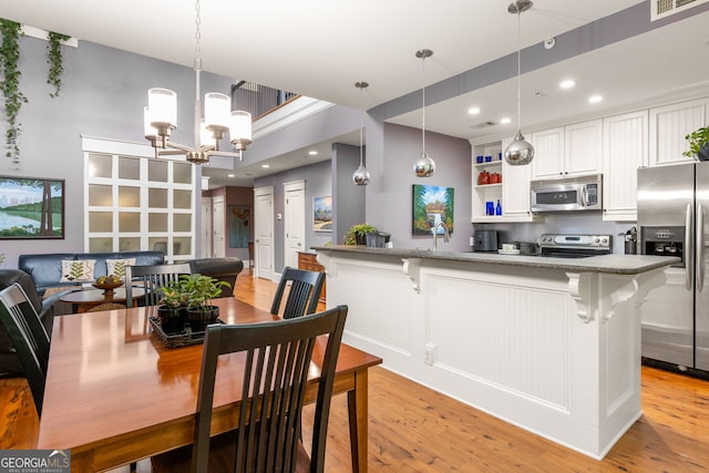 kitchen with light wood finished floors, stainless steel appliances, open shelves, a breakfast bar area, and white cabinetry