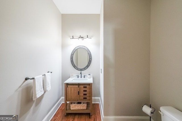 half bathroom featuring wood finished floors, vanity, toilet, and baseboards