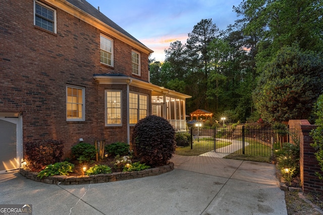 property exterior at dusk with fence, a sunroom, and brick siding