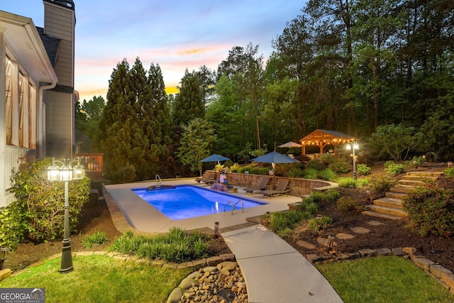 pool at dusk with stairway, an outdoor pool, and a patio