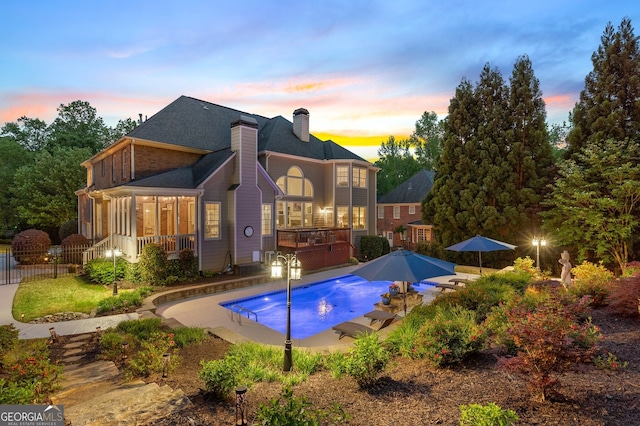 pool at dusk featuring fence, an outdoor pool, a patio, and a deck