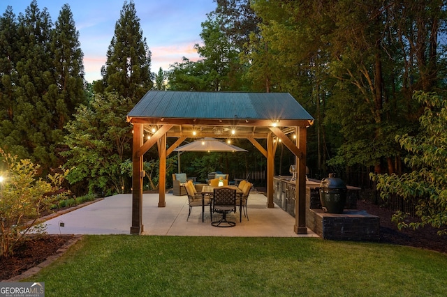 patio terrace at dusk featuring a gazebo, an outdoor kitchen, and a lawn