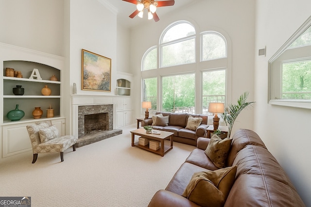 carpeted living area with visible vents, built in features, a fireplace with raised hearth, a high ceiling, and ceiling fan
