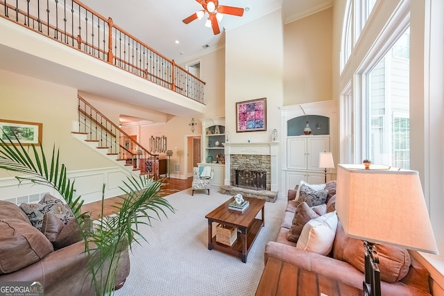living area with a high ceiling, crown molding, carpet flooring, stairs, and ceiling fan