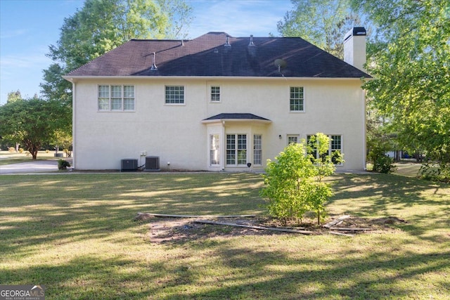 back of house with a chimney, a lawn, central air condition unit, and stucco siding