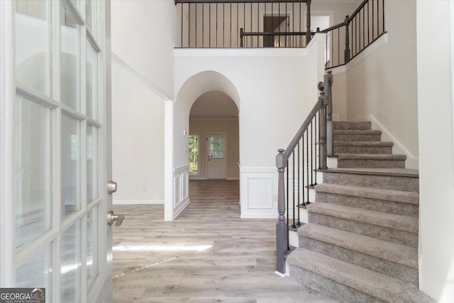 entryway featuring a towering ceiling, wood finished floors, stairs, arched walkways, and baseboards