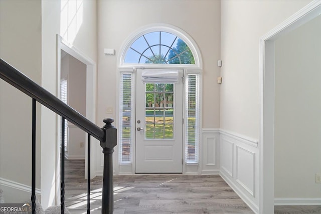 foyer entrance with wood finished floors, wainscoting, and stairway
