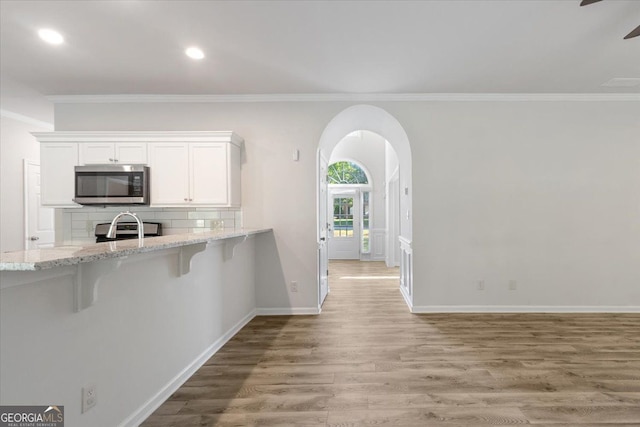 kitchen featuring stainless steel microwave, ornamental molding, light wood-type flooring, white cabinetry, and light stone countertops