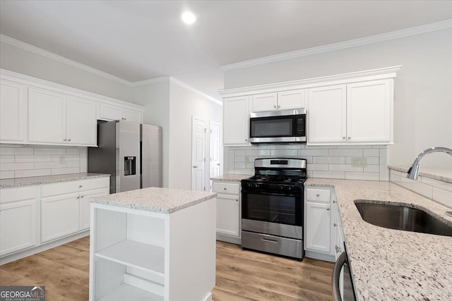 kitchen featuring appliances with stainless steel finishes, a sink, crown molding, white cabinets, and decorative backsplash