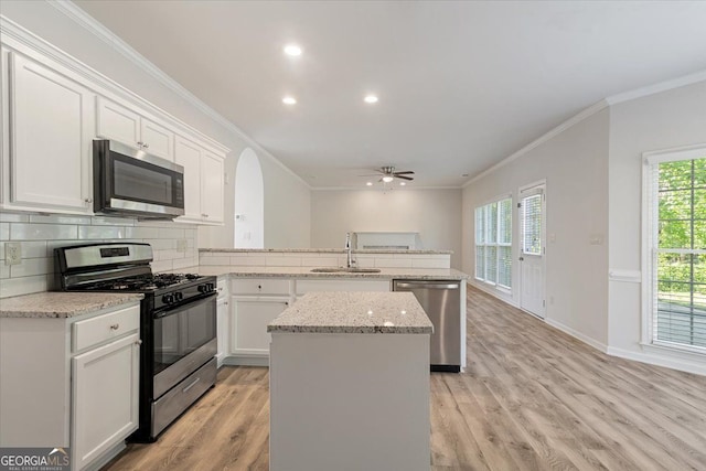 kitchen with stainless steel appliances, a sink, a peninsula, crown molding, and white cabinetry