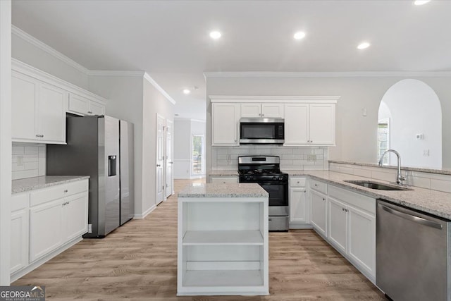 kitchen with appliances with stainless steel finishes, a sink, crown molding, arched walkways, and white cabinetry
