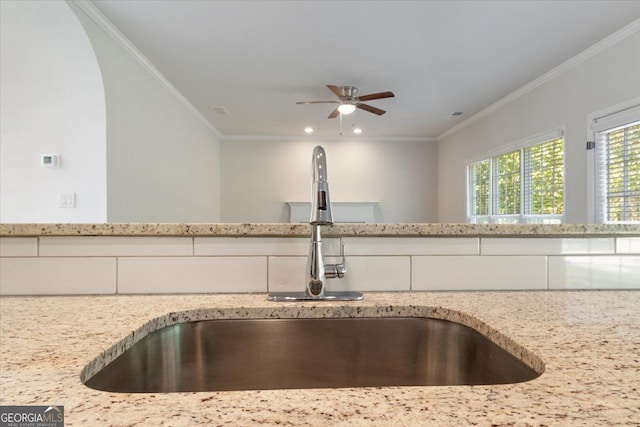 kitchen view of a sink, light stone counters, ornamental molding, a ceiling fan, and recessed lighting