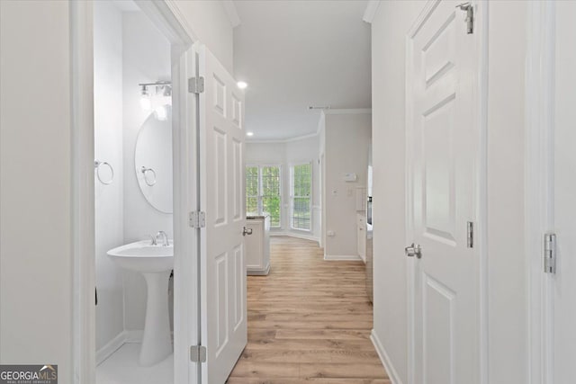 corridor featuring crown molding, baseboards, light wood-style flooring, and a sink