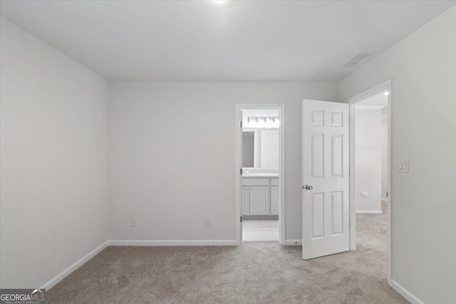 unfurnished bedroom with light carpet, baseboards, and ensuite bathroom