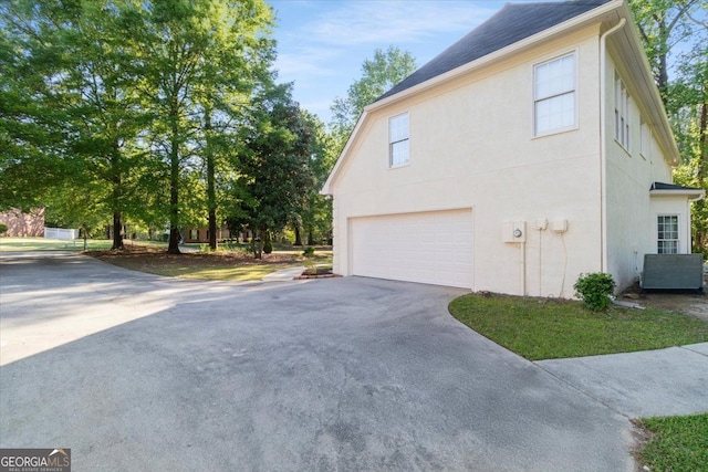 view of side of home with a garage, driveway, stucco siding, and a shingled roof