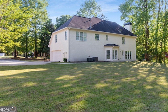 back of property with a chimney, an attached garage, stucco siding, and a yard