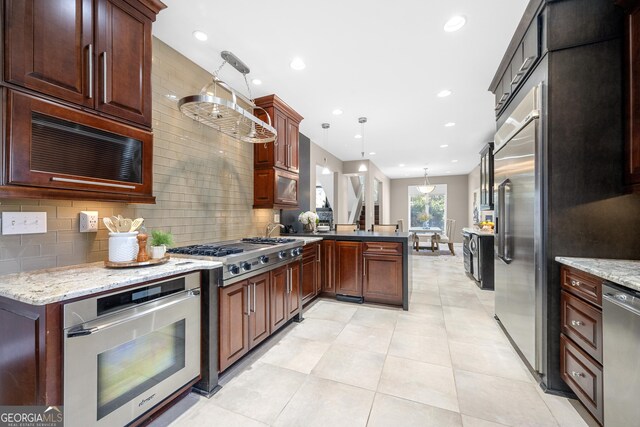 kitchen with light stone counters, decorative backsplash, decorative light fixtures, a peninsula, and appliances with stainless steel finishes