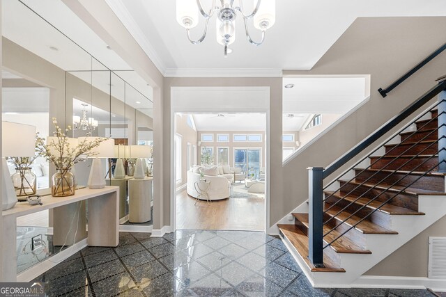 foyer entrance featuring crown molding, stairs, granite finish floor, baseboards, and a notable chandelier