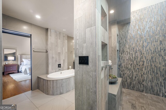 ensuite bathroom with tile walls, a garden tub, connected bathroom, and a walk in shower