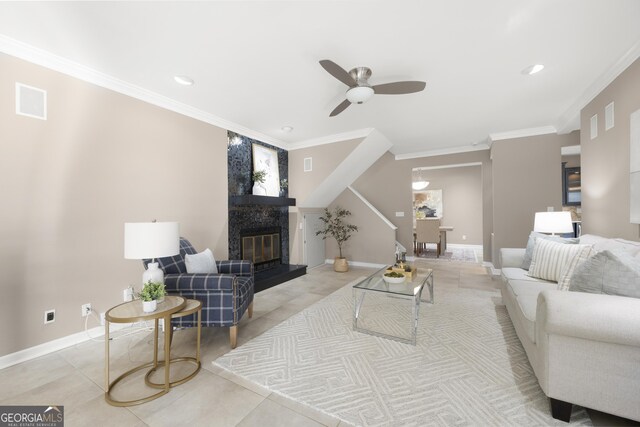 living area featuring ornamental molding, a ceiling fan, a glass covered fireplace, and light tile patterned floors