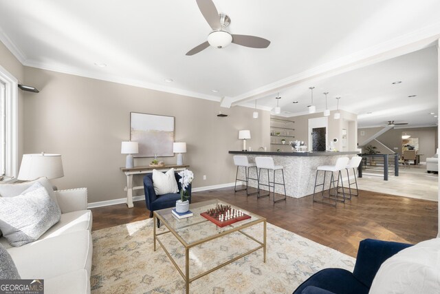 living room with wood finished floors, a ceiling fan, baseboards, and ornamental molding