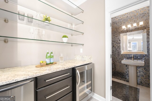 bar featuring wine cooler, stainless steel dishwasher, a sink, light tile patterned flooring, and a bar