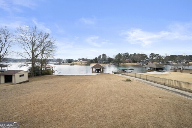 exterior space featuring a shed, a dock, a water view, fence, and an outbuilding