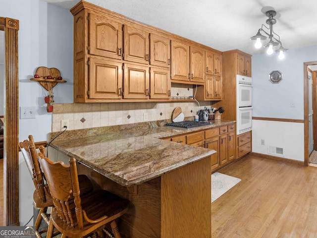 930 Singley Dr, Locust Grove, GA 30248 - kitchen featuring light wood finished floors, a peninsula, stainless steel gas cooktop, decorative backsplash, and double oven
