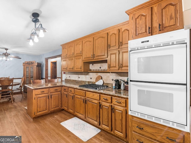 930 Singley Dr, Locust Grove, GA 30248 - kitchen with backsplash, white double oven, light wood-style floors, stainless steel gas cooktop, and a peninsula