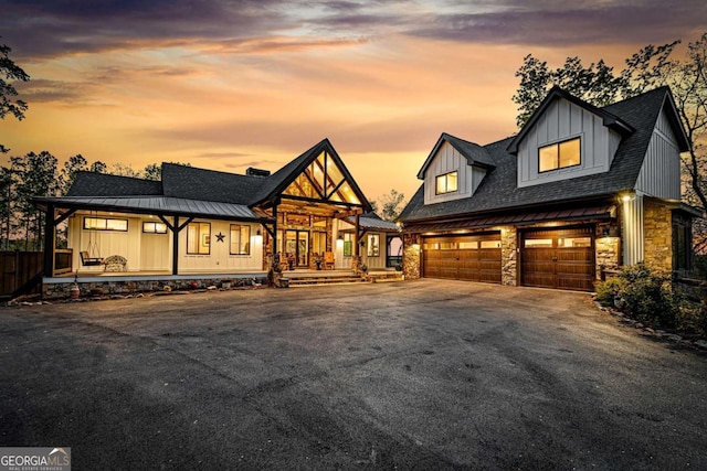 modern farmhouse style home featuring stone siding, covered porch, aphalt driveway, and a garage