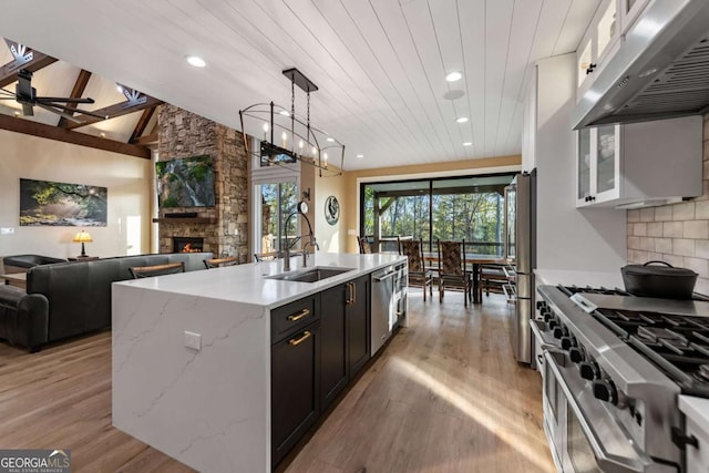 kitchen featuring a sink, open floor plan, under cabinet range hood, a stone fireplace, and appliances with stainless steel finishes
