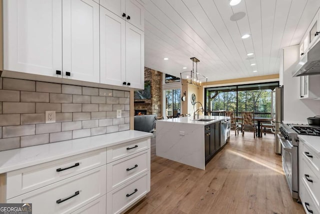 kitchen with white cabinetry, light wood-style floors, a fireplace, an island with sink, and appliances with stainless steel finishes
