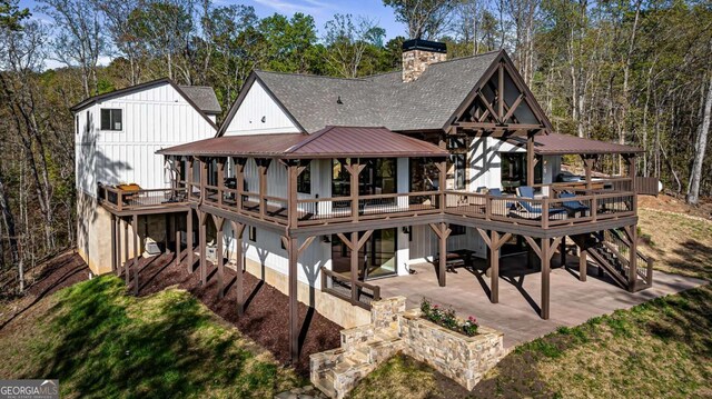 back of house with a wooden deck, a patio area, roof with shingles, and a chimney