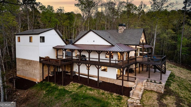 back of house at dusk with a wooden deck, stairway, and metal roof